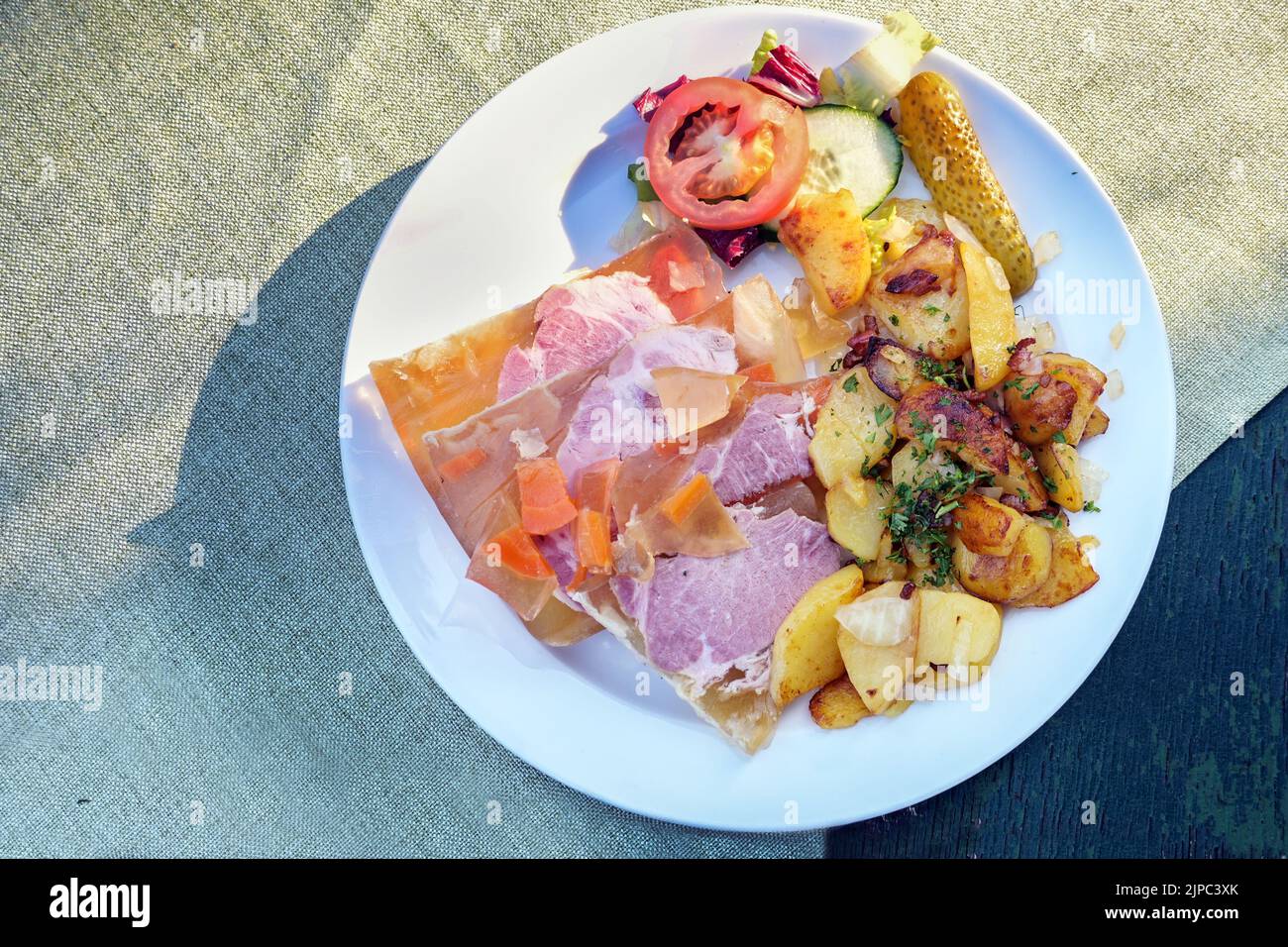 Sauerfleisch mit Bratkartoffeln or sour pickled meat in aspic with fried potatoes, traditional German and Austrian dish on a white plate and a rustic Stock Photo