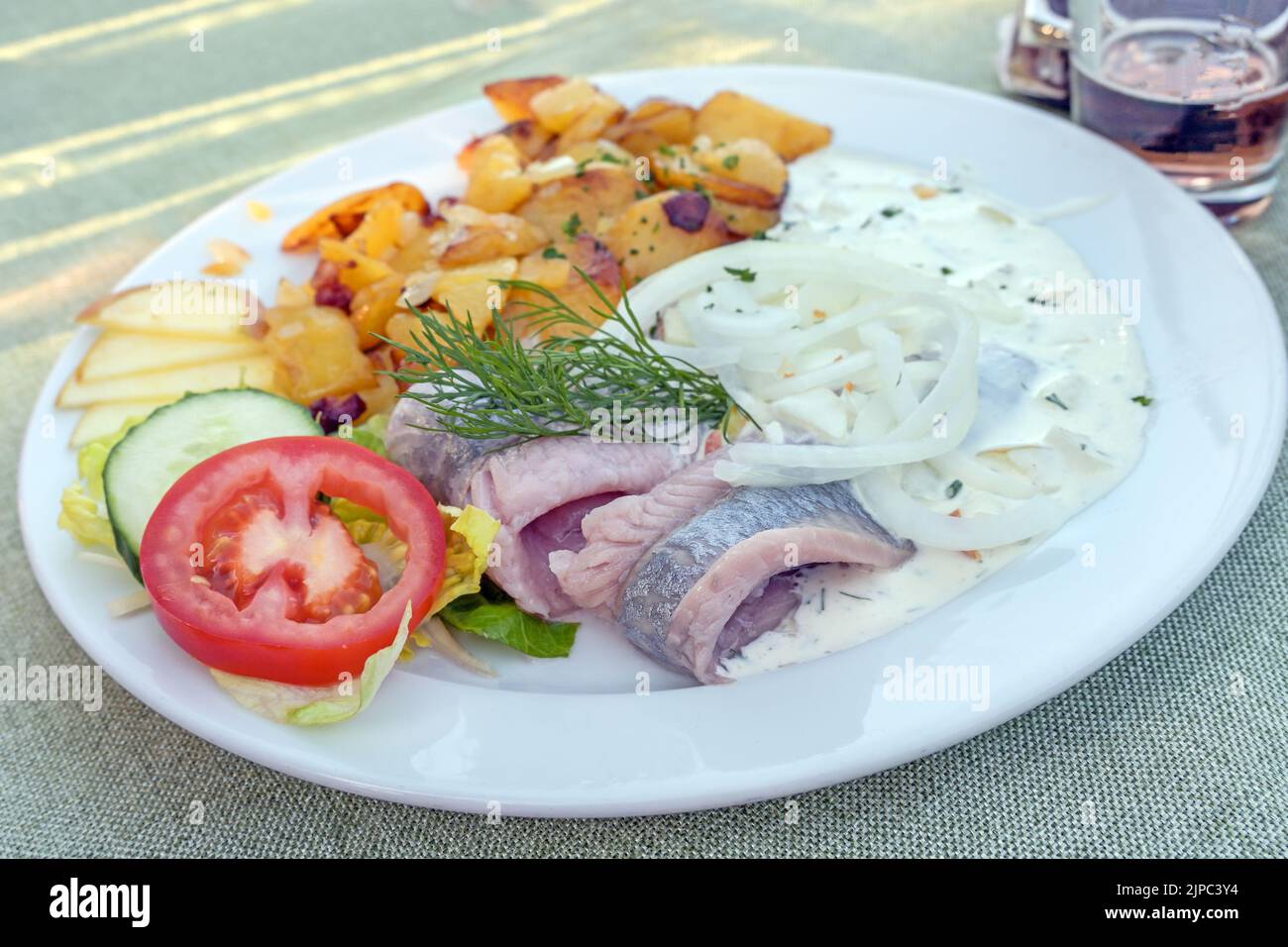 Pickled herring or matjes fillet with cream sauce and onions, served with fried potatoes and salad on a white plate, copy space, selected focus, narro Stock Photo