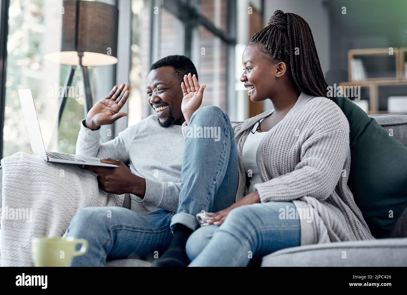 Happy couple waving while talking on video call and online chat on a laptop webcam in a lounge at home. Smiling man and woman having conversation Stock Photo