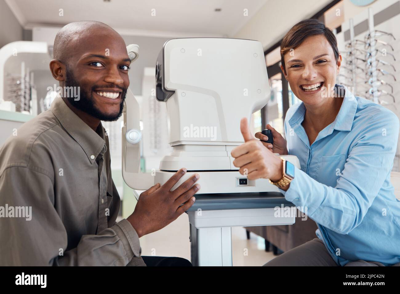 Eye doctor giving thumbs up after a successful vision test with a happy male patient, portrait. Smiling female optometrist gives a positive gesture Stock Photo