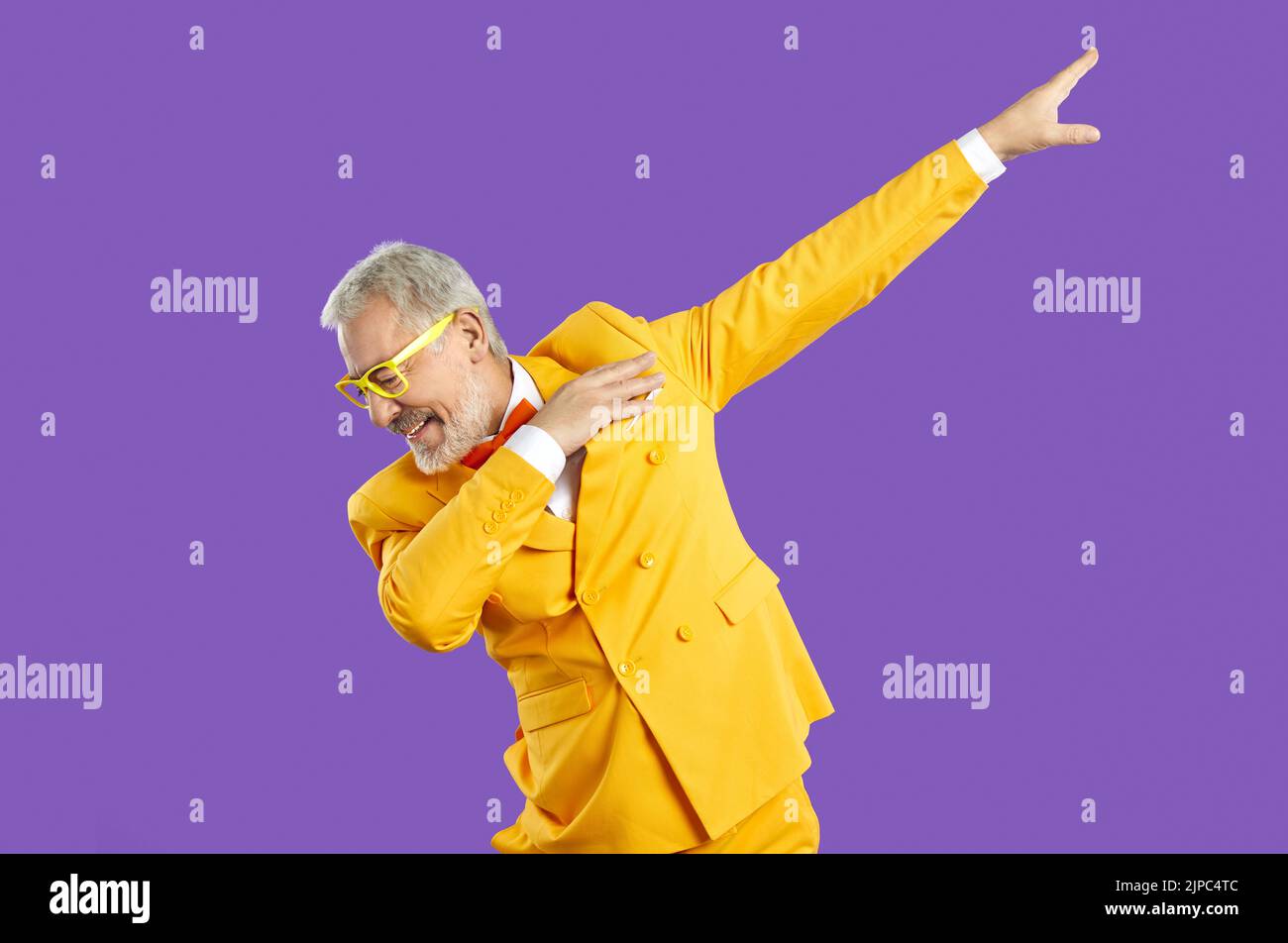 Portrait of funny senior man in yellow suit dancing isolated on purple