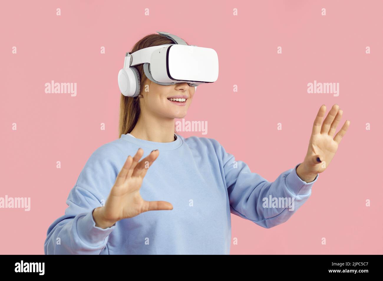 Smiling amazed young woman touching air during VR experience, isolated on pink background. Stock Photo