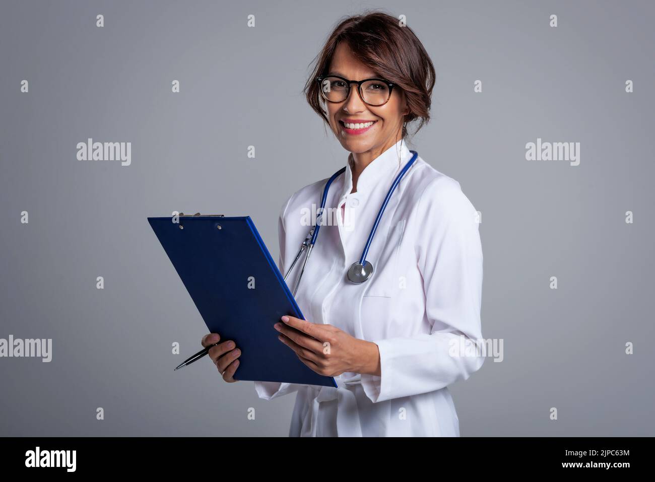 Smiling female doctor holding clipboard in her hand while looking at ...