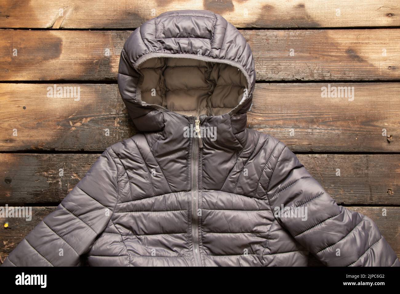 Gray women's warm winter jacket lies on a wooden table, fashionable outerwear Stock Photo