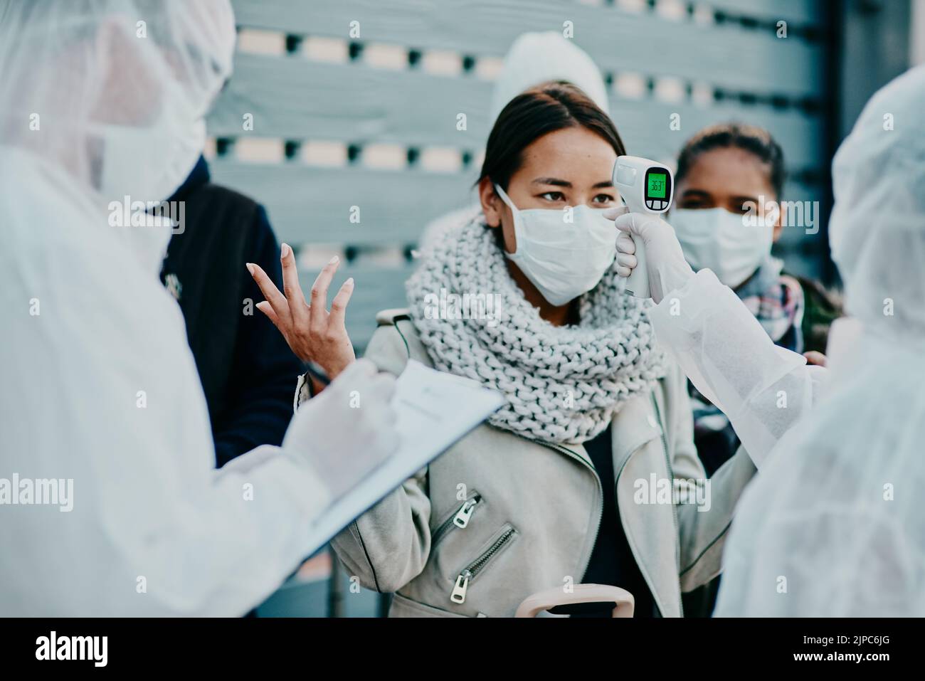 Health care worker scanning a frustrated woman temperature for corona with a thermometer. Concerned female made victim of racial profiling, looking Stock Photo