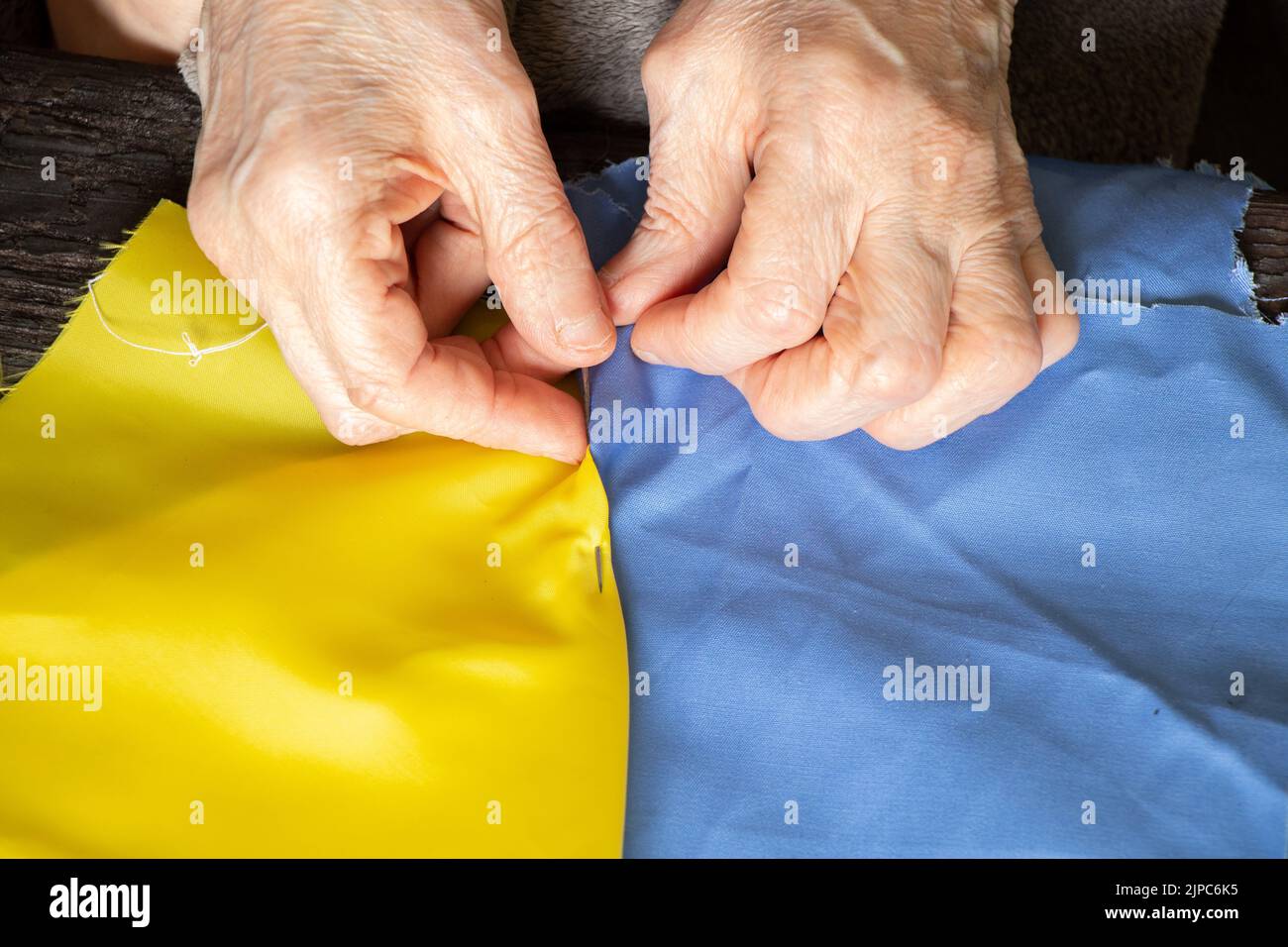 Female old Ukrainian woman hands sew the national flag of Ukraine
