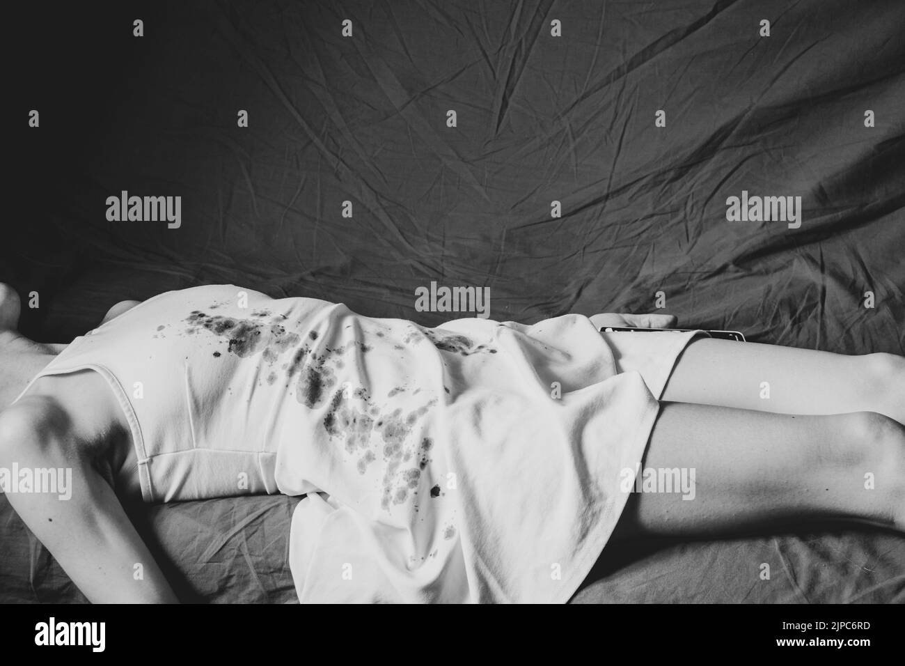A murdered and tortured Ukrainian woman in a white dress and bloodstains lies on a bed at home, a protest action of Ukrainian women protecting women Stock Photo