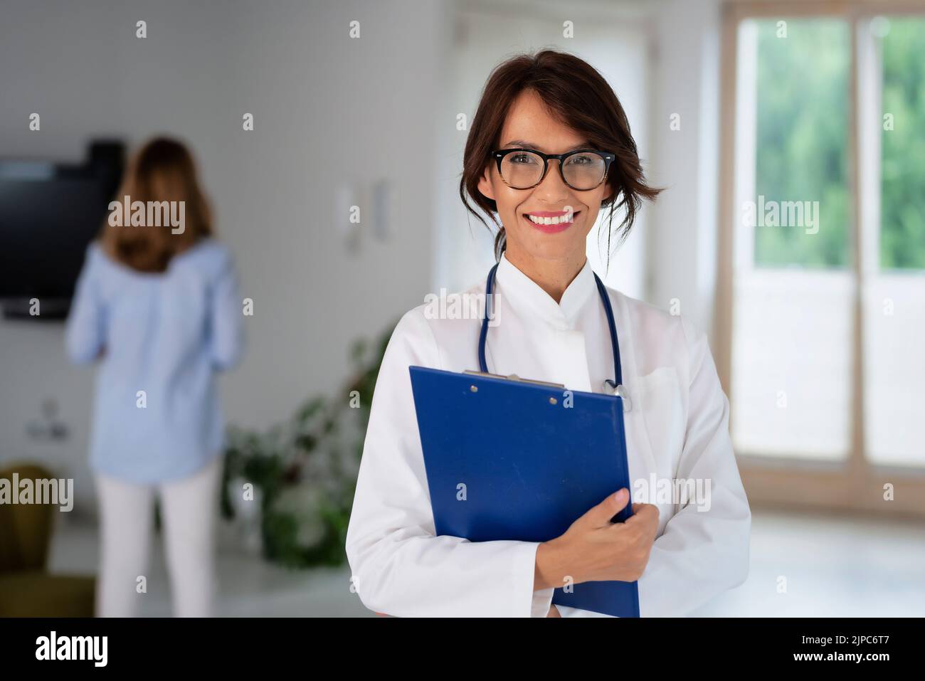 Female doctor wearing lab coat and stethoscope and holding clipboard in her hands while standing