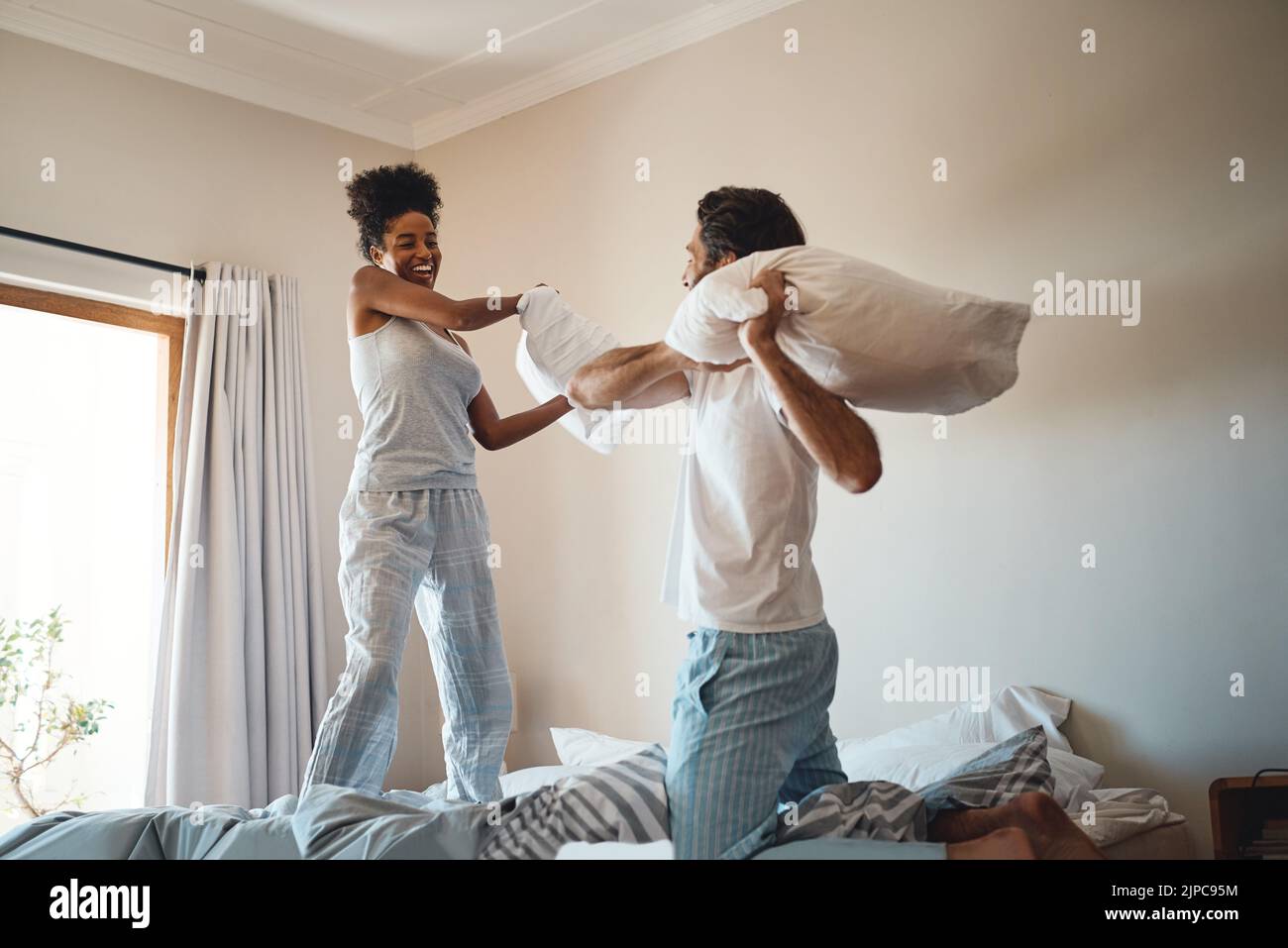 Pillow fight, playing and bonding with a happy couple playing, bonding and spending time together in their bedroom at home. Laughing, having fun and Stock Photo