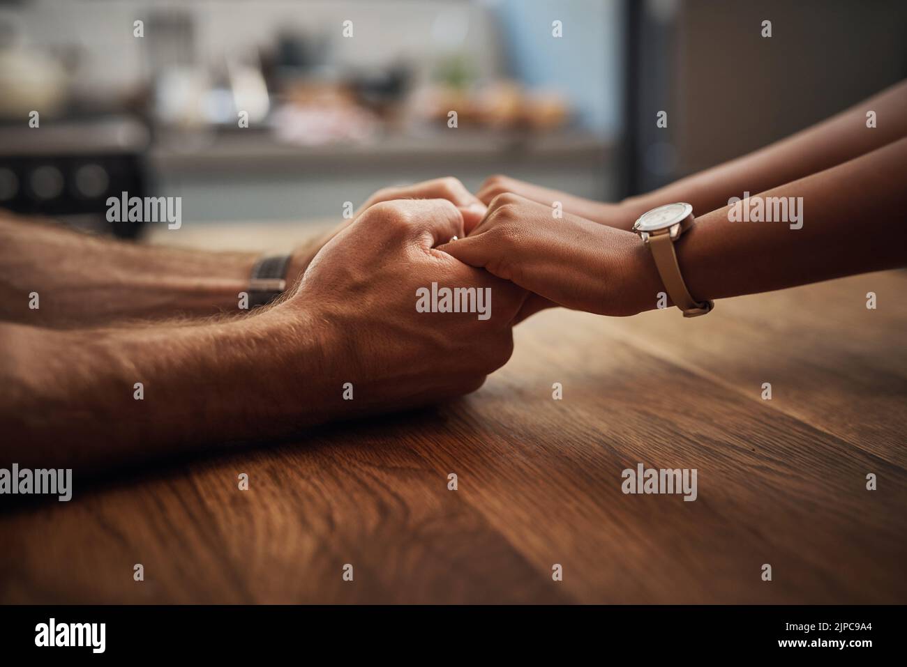 Couple holding hands in support, grief and healing together on a wooden table at home. Closeup of a caring partner in sorrow due to cancer and Stock Photo