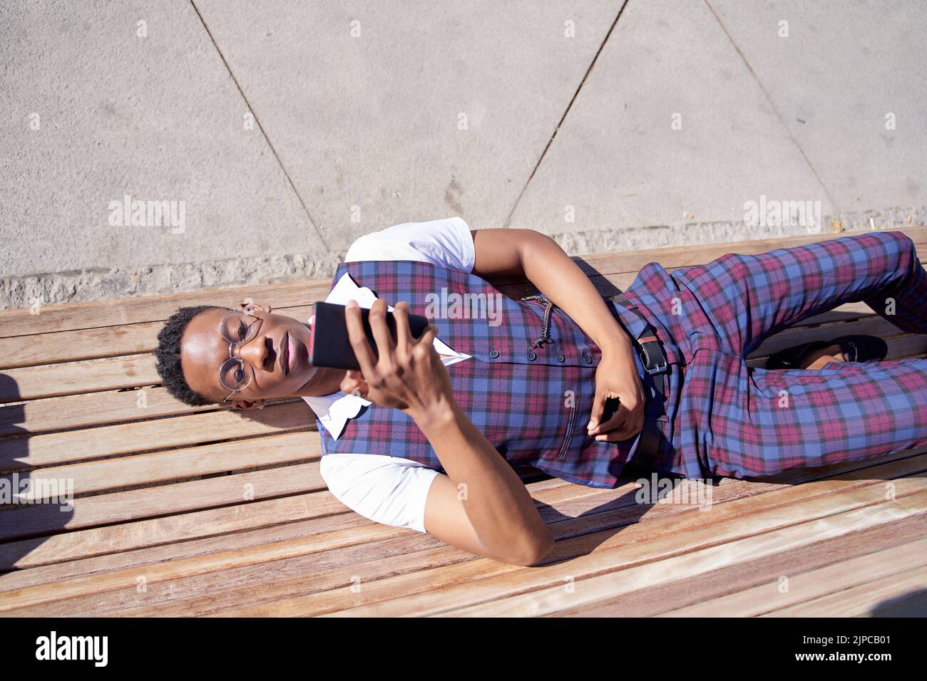 Man african american businessman lying on a bench and resting after work uses a mobile phone Stock Photo