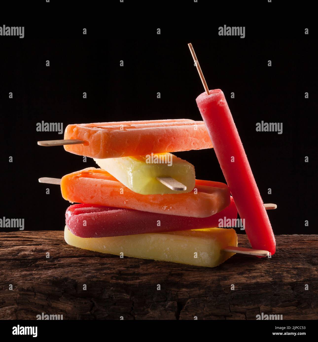 A pile of ice lollies of different flavors on a wooden surface. Stock Photo