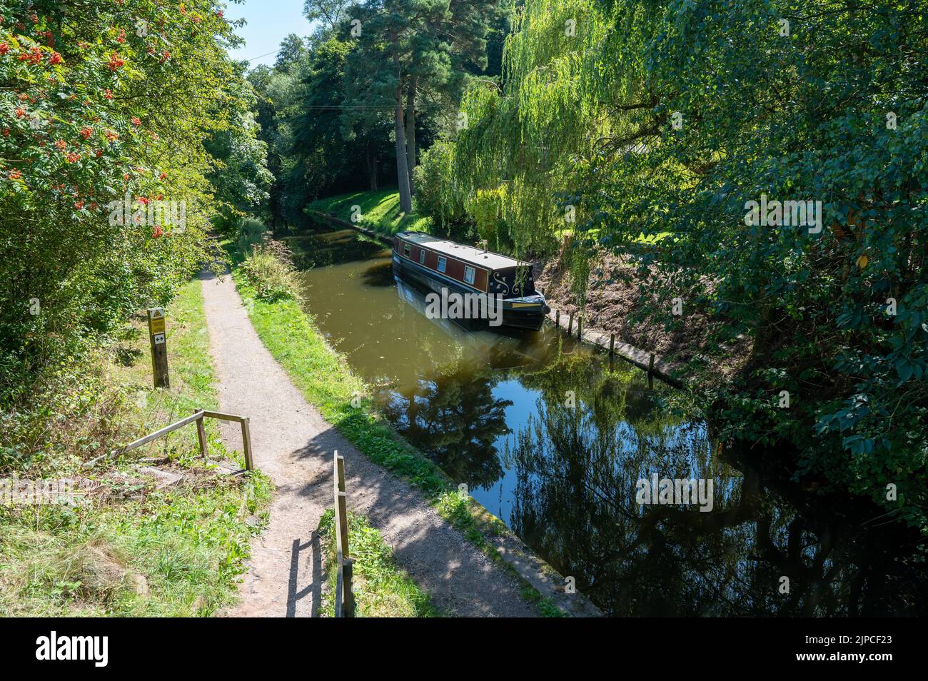Narrowboat moored on the Caldon canal in Staffordshire in bright sunshine amongst trees and shrubs. Stock Photo