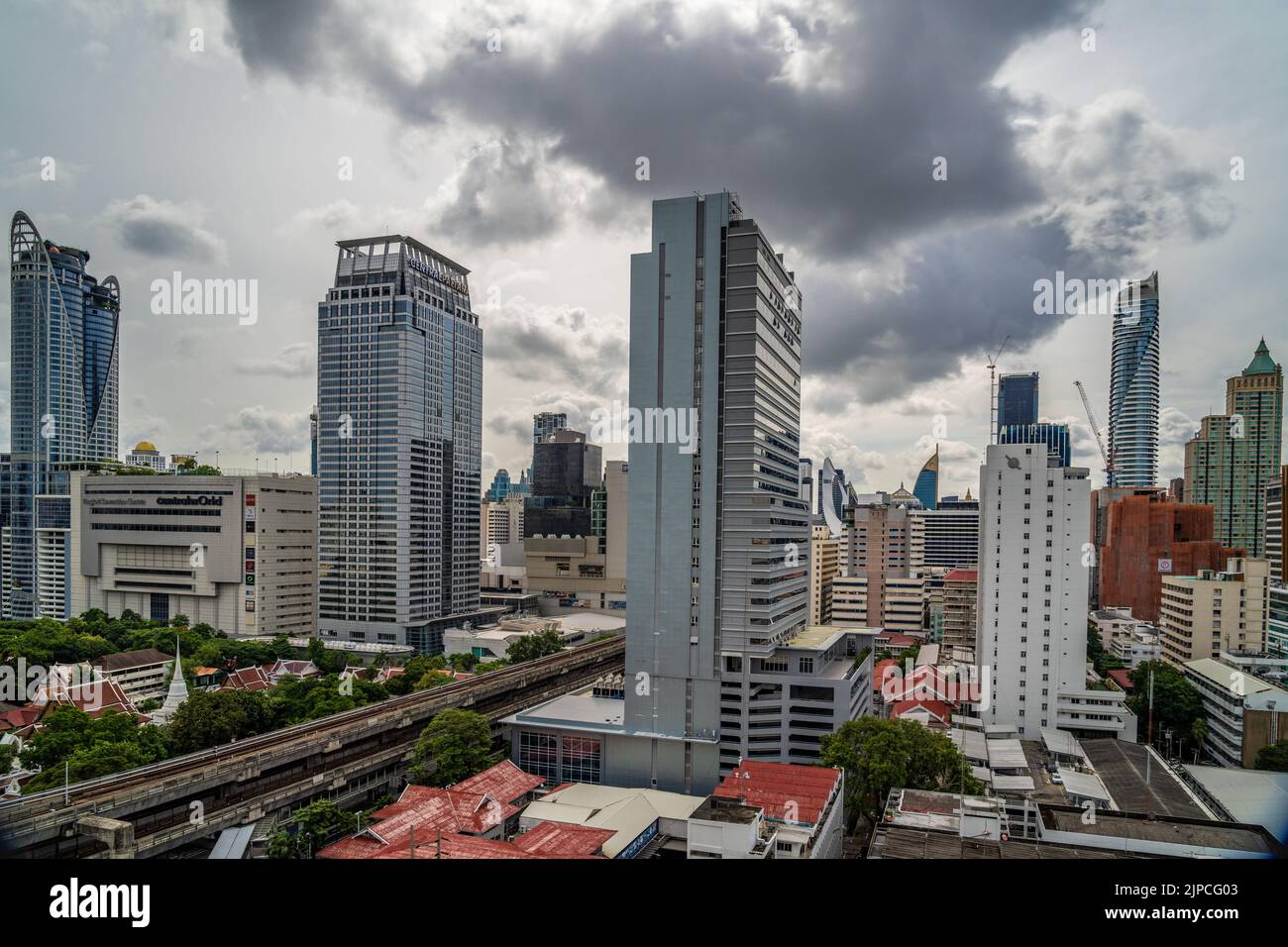 Bangkok, Thailand - 12 August 2022 - Aerial view of Bangkok cityscape showing high-rises and running BTS skytrains with cloudy blue sky Stock Photo