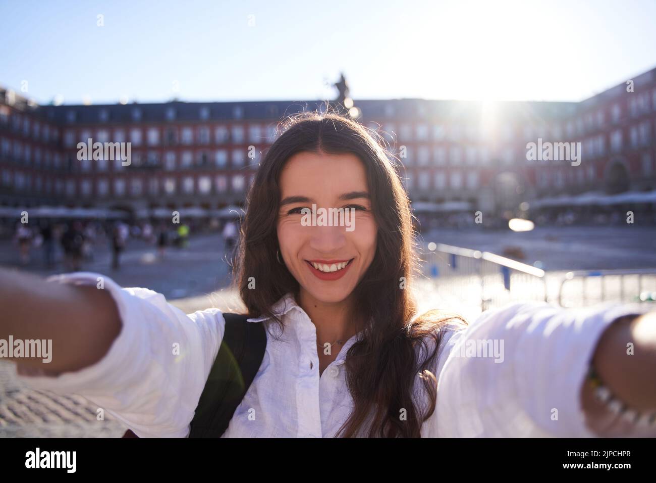 Happy caucasian woman is taking a selfie smiling at the camera in front of the Equestrian Monument to King Felipe III of Spain in the Plaza Mayor in M Stock Photo