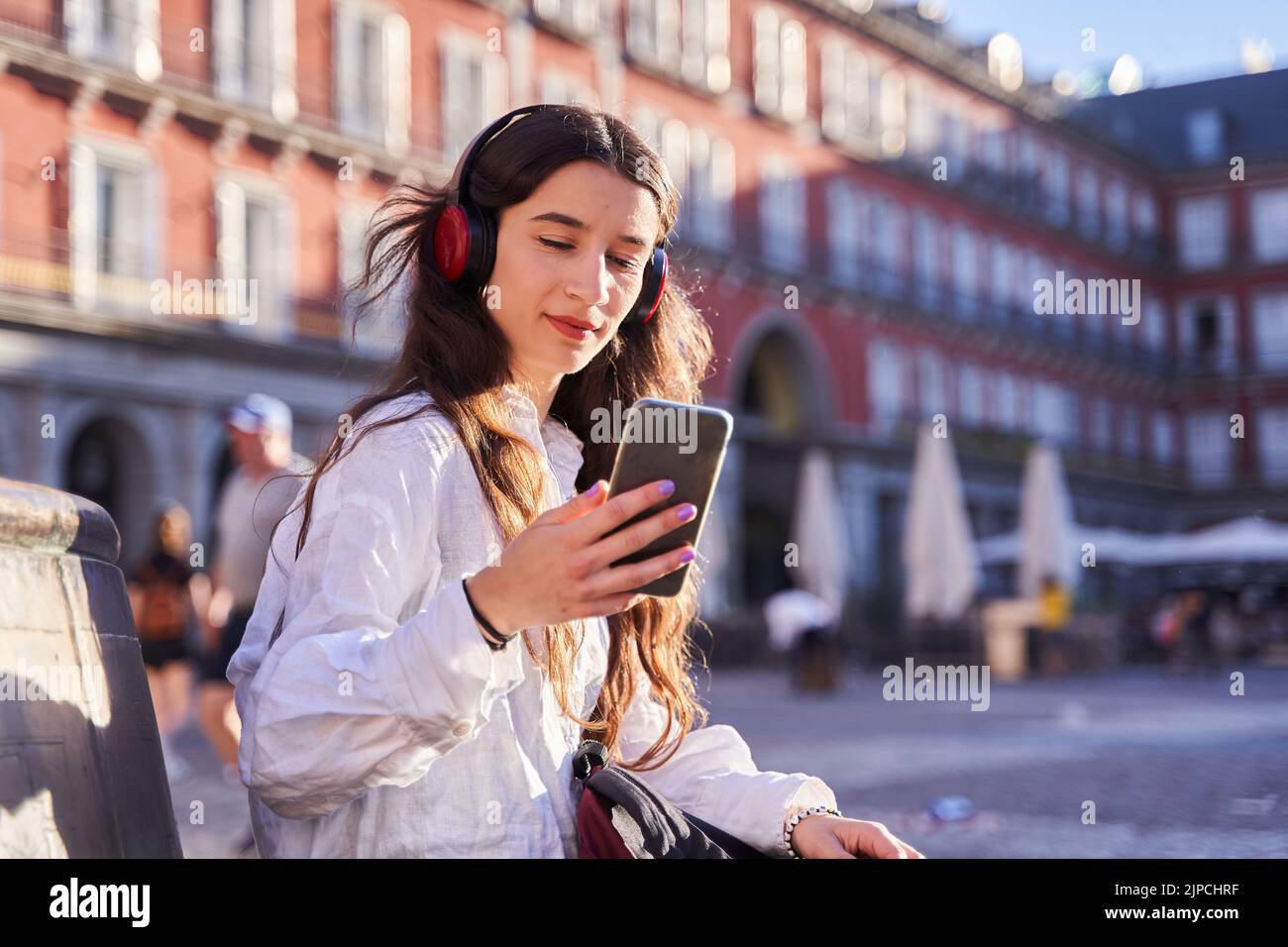 portrait of a young woman looking at a smart phone sitting in Madrid. Stock Photo
