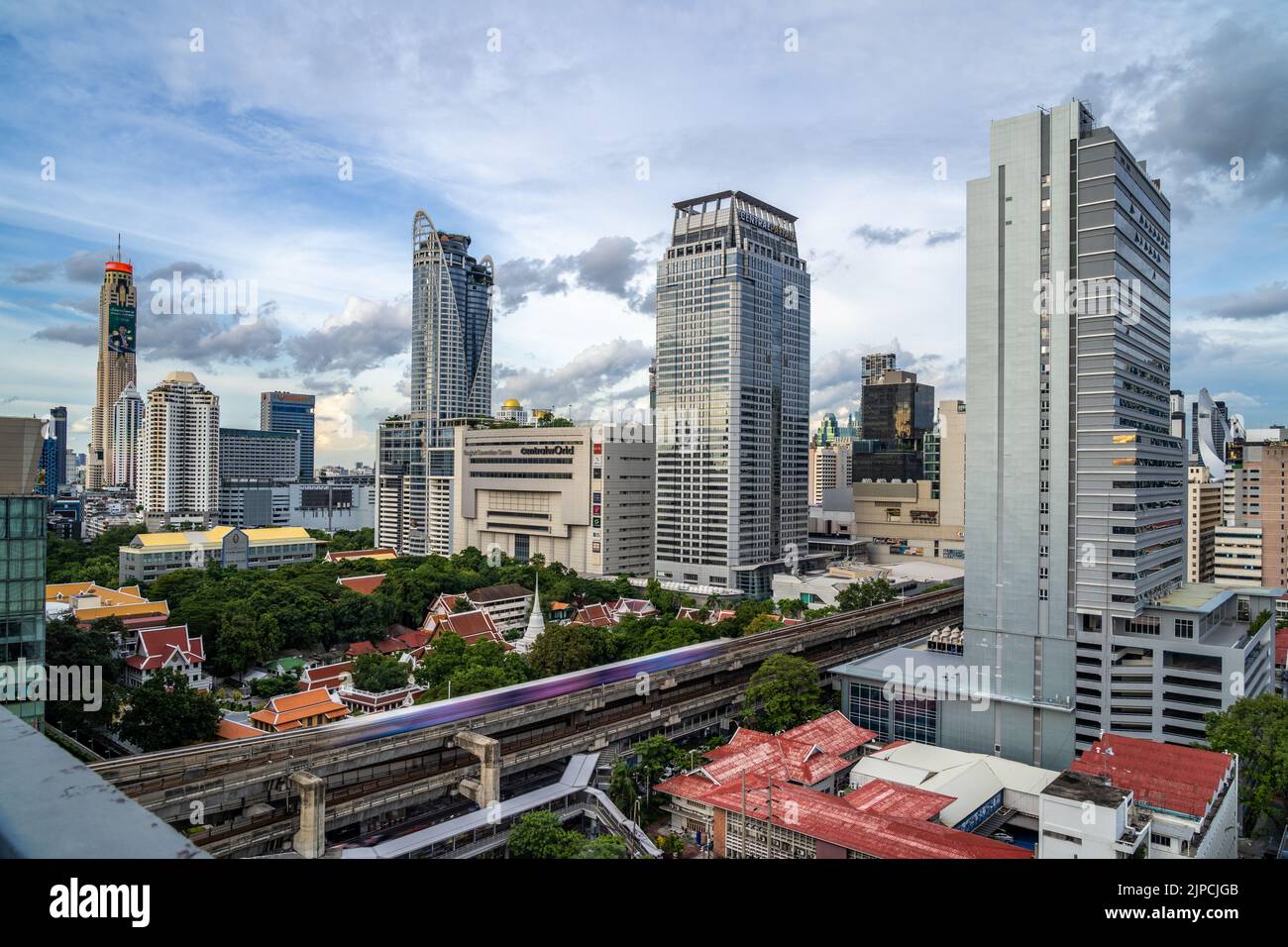 Bangkok, Thailand - 10 August 2022 - Aerial view of Bangkok cityscape showing high-rises and running BTS skytrains with cloudy blue sky Stock Photo
