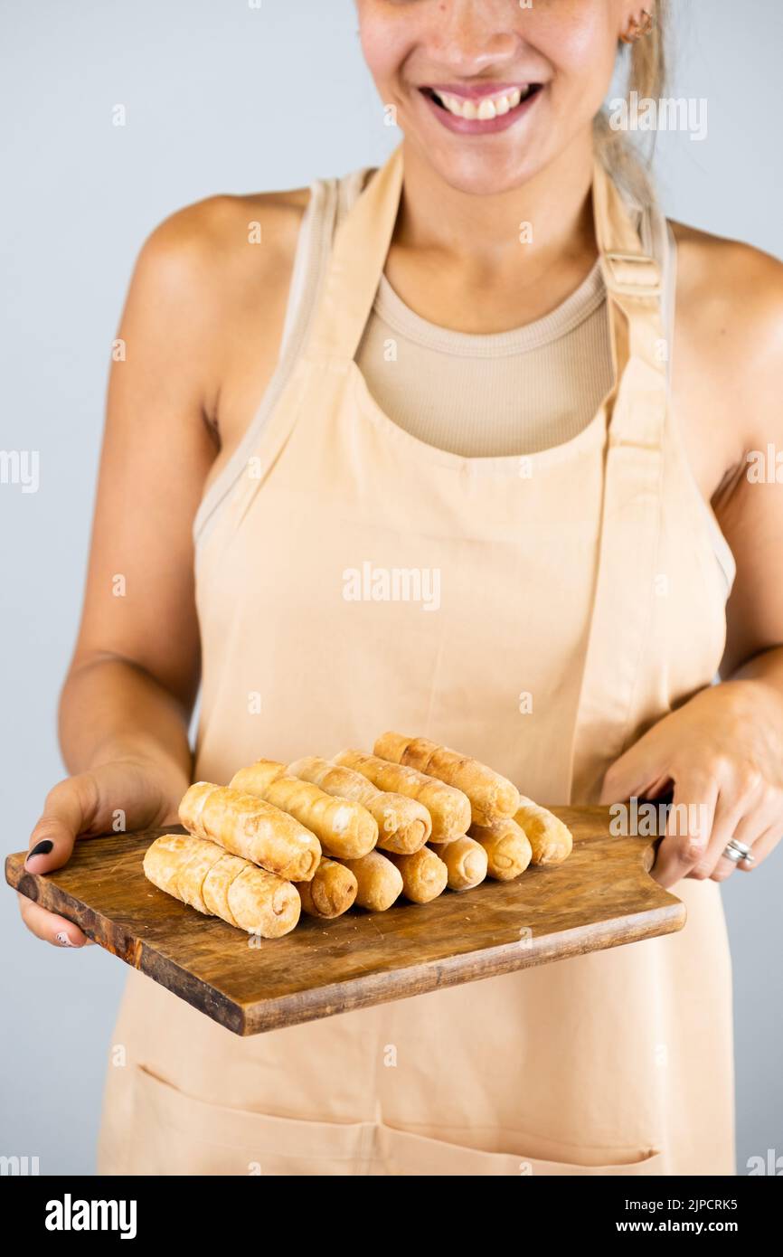 Latin girl holding a wooden board with freshly cooked tequeños, typical Venezuelan food Stock Photo