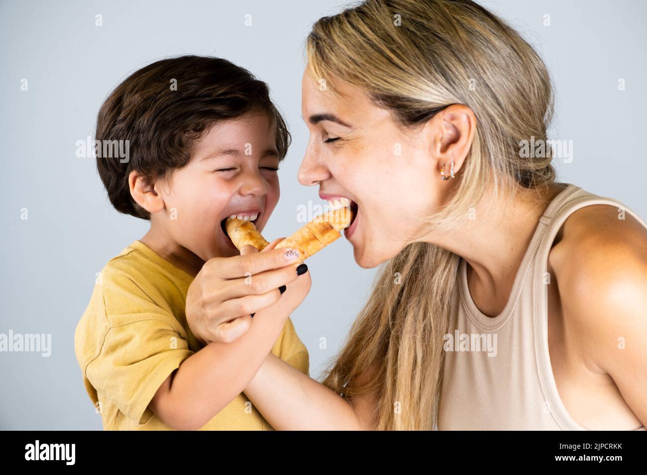 Mother and son enjoying and eating a Latin American snack called tequeños, funny expressions on their faces Stock Photo