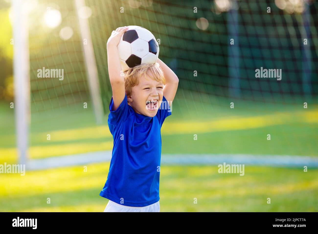 Kids play football on outdoor stadium field. Children score a goal