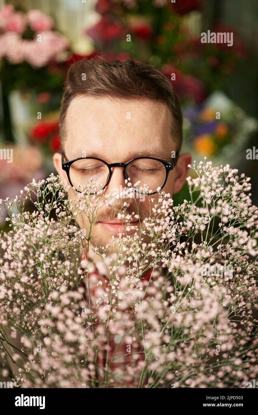 Closeup portrait of cheerful male person wearing eyeglasses sniffing fresh spring daisy flower bouquet with closed eyes. Mother's Day, Valentine's Day or International Women's Day concept Stock Photo