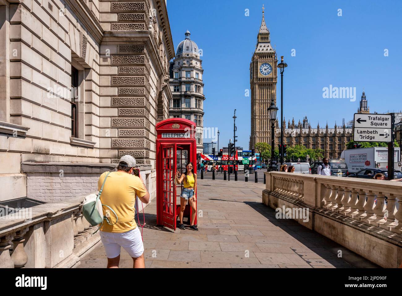 Tourists Pose For Photos Outside A Traditional Red Telephone Box In Parliament Square During A Heatwave, London, UK. Stock Photo