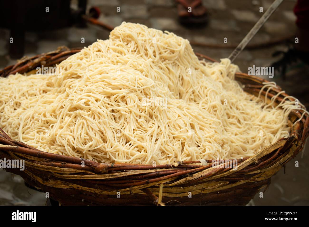 Chinese Schezwan Also Called Szechwan Veg Hakka Noodles Chowmin or Indian Veg Chow Mein Being Washed Rinsed In Water In Bamboo Basket. Dhaba Style Stock Photo