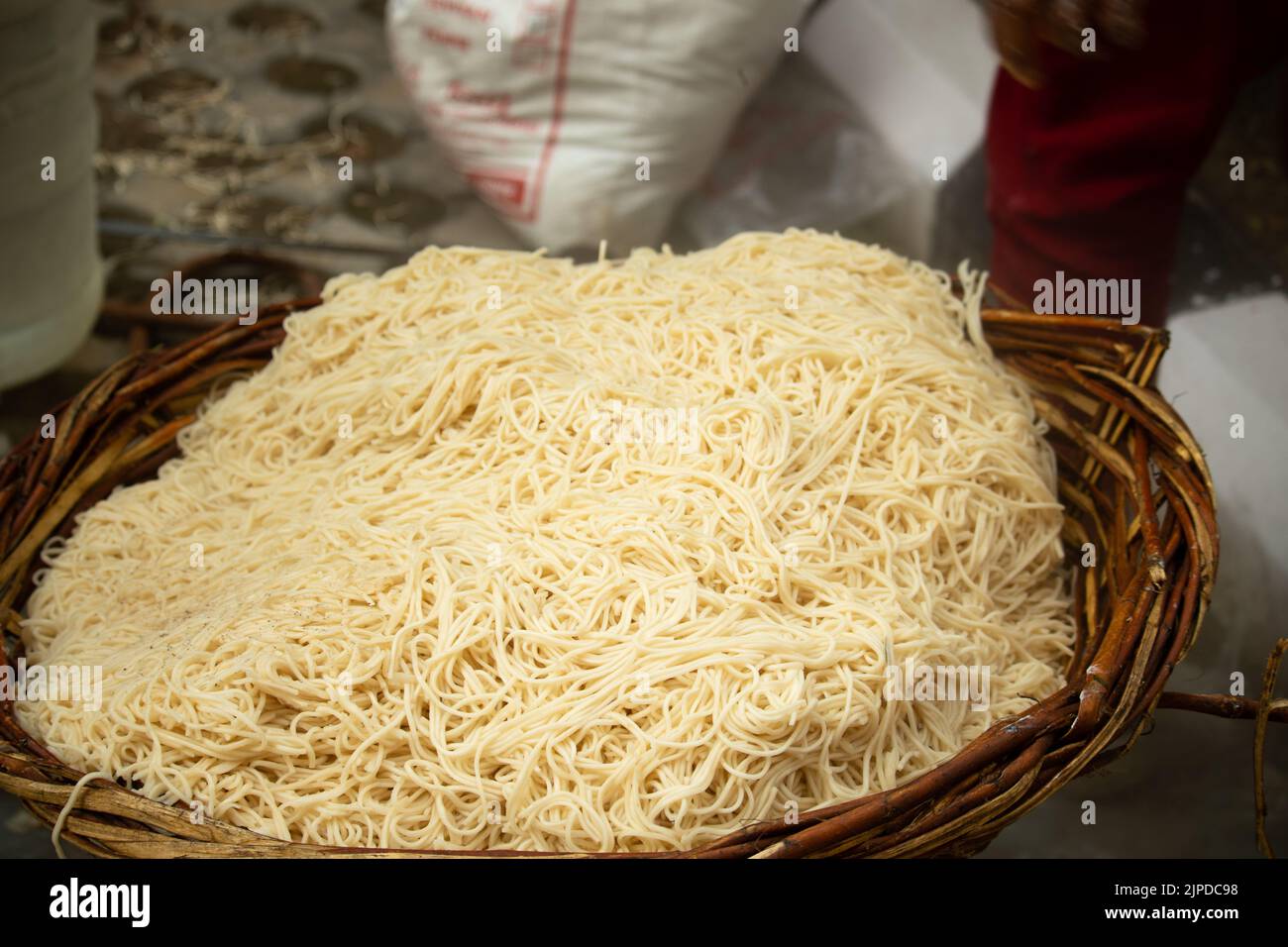Chinese Schezwan Also Called Szechwan Veg Hakka Noodles Chowmin or Indian Veg Chow Mein Being Washed Rinsed In Water In Bamboo Basket. Dhaba Style Stock Photo