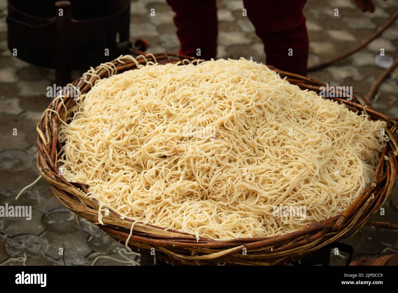 Chinese Schezwan Also Called Szechwan Veg Hakka Noodles Chowmin or Indian Veg Chow Mein Being Washed Rinsed In Water In Bamboo Basket. Dhaba Style Stock Photo