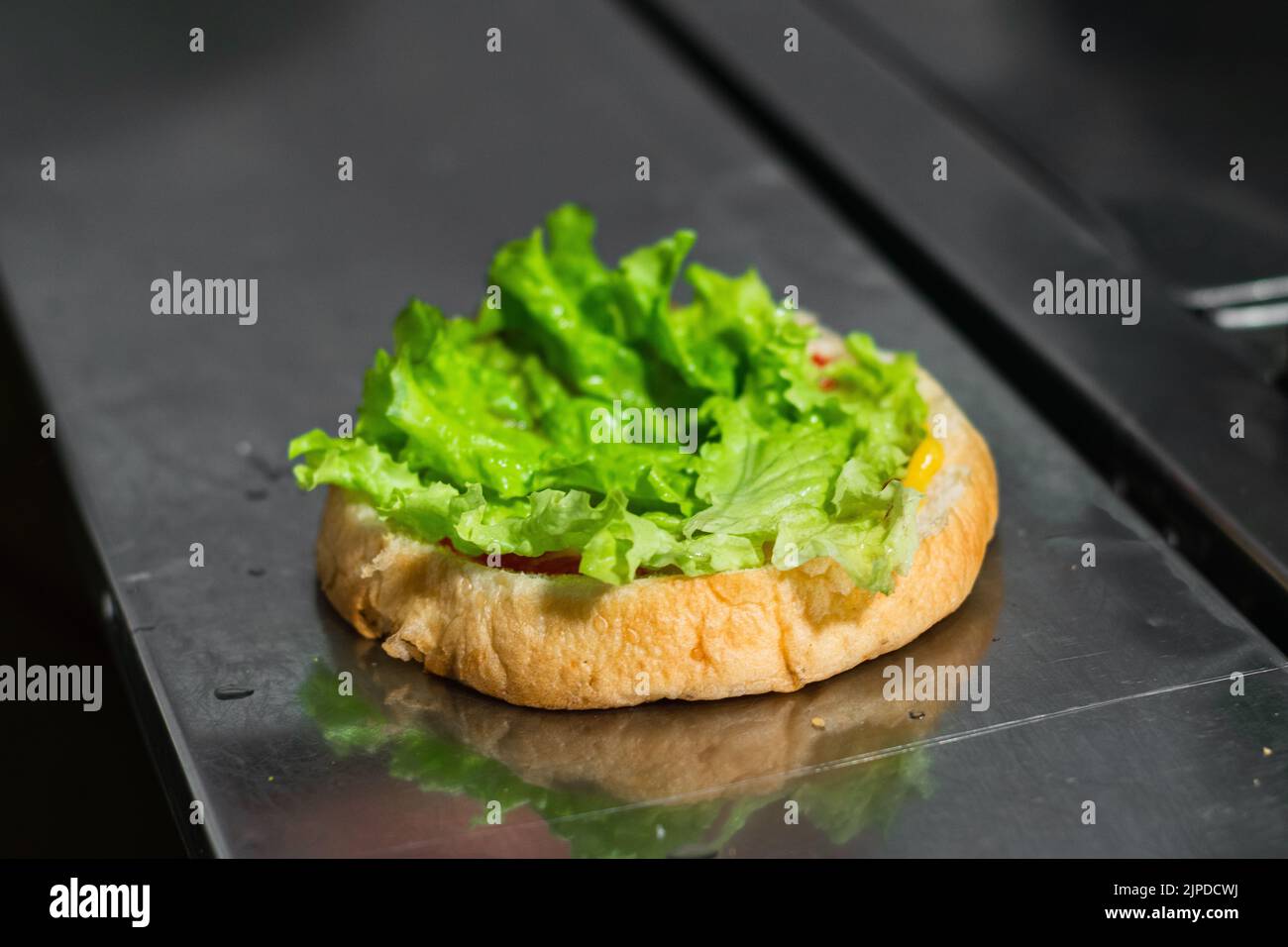 close-up of the beginning of the preparation of a colombian hamburger, in a fast food stand located on the street. bread and lettuce on a metal table. Stock Photo