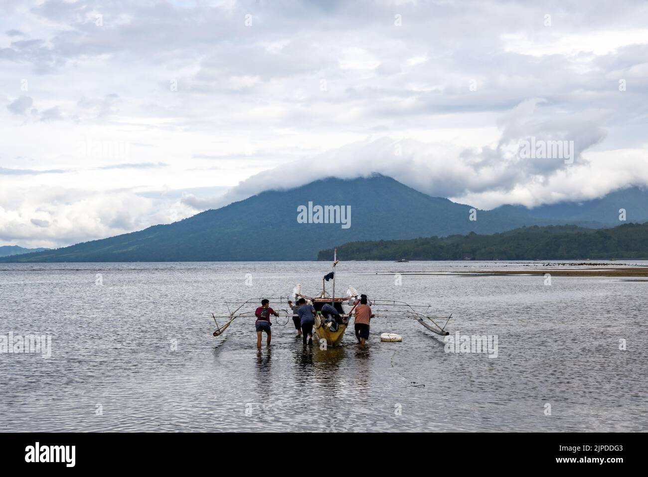Three men pushing an outrigger boat out to sea. Sulawesi, Indonesia. Stock Photo