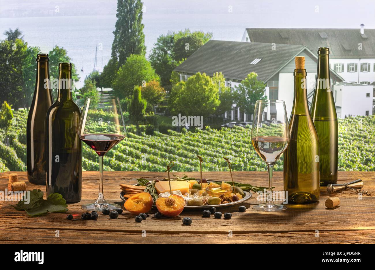 Bottles and glasses of red and white wine with delicious appetizers, olives, cheese and honey, fruits and berries lying on table. Countryside vineyard Stock Photo
