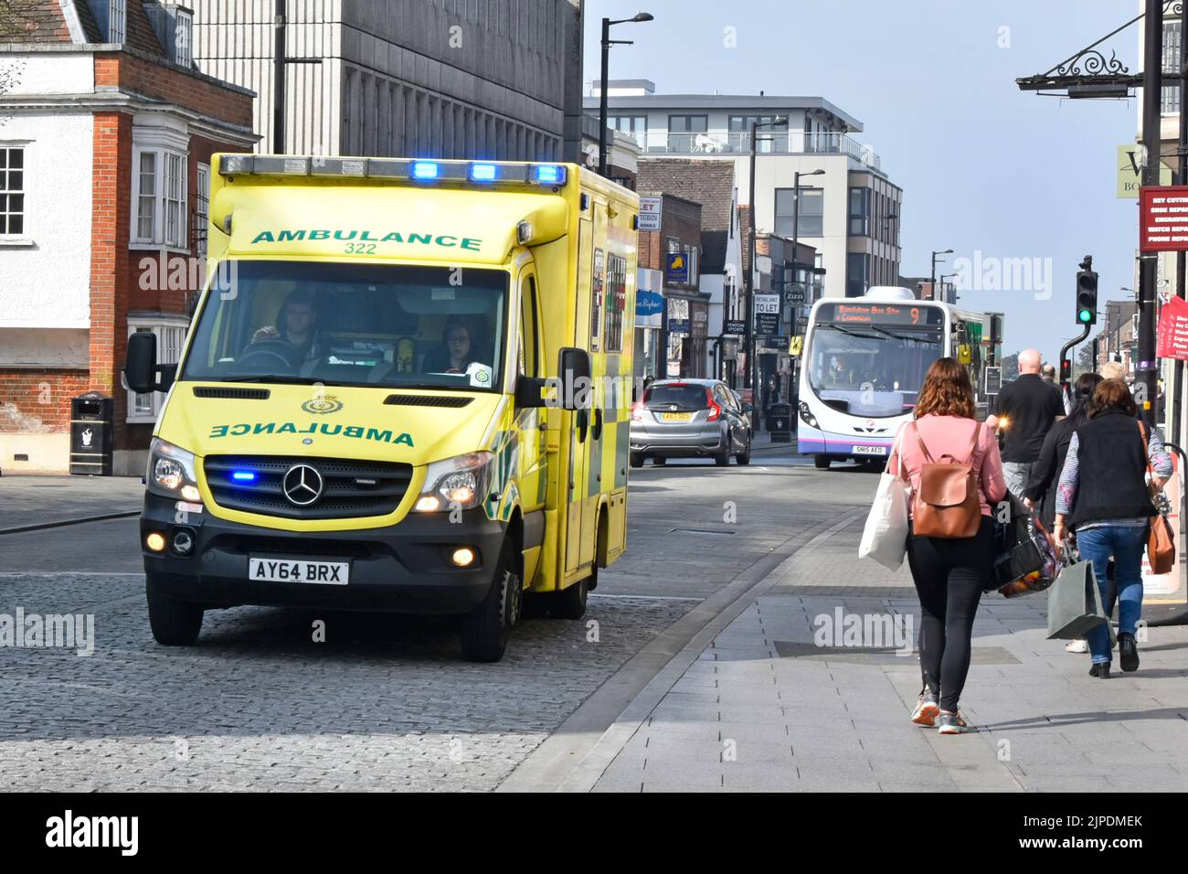East of England blue lights Emergency Ambulance Service NHS vehicle & crew on 999 journey shoppers & bus in High Street  Brentwood Essex England  UK Stock Photo