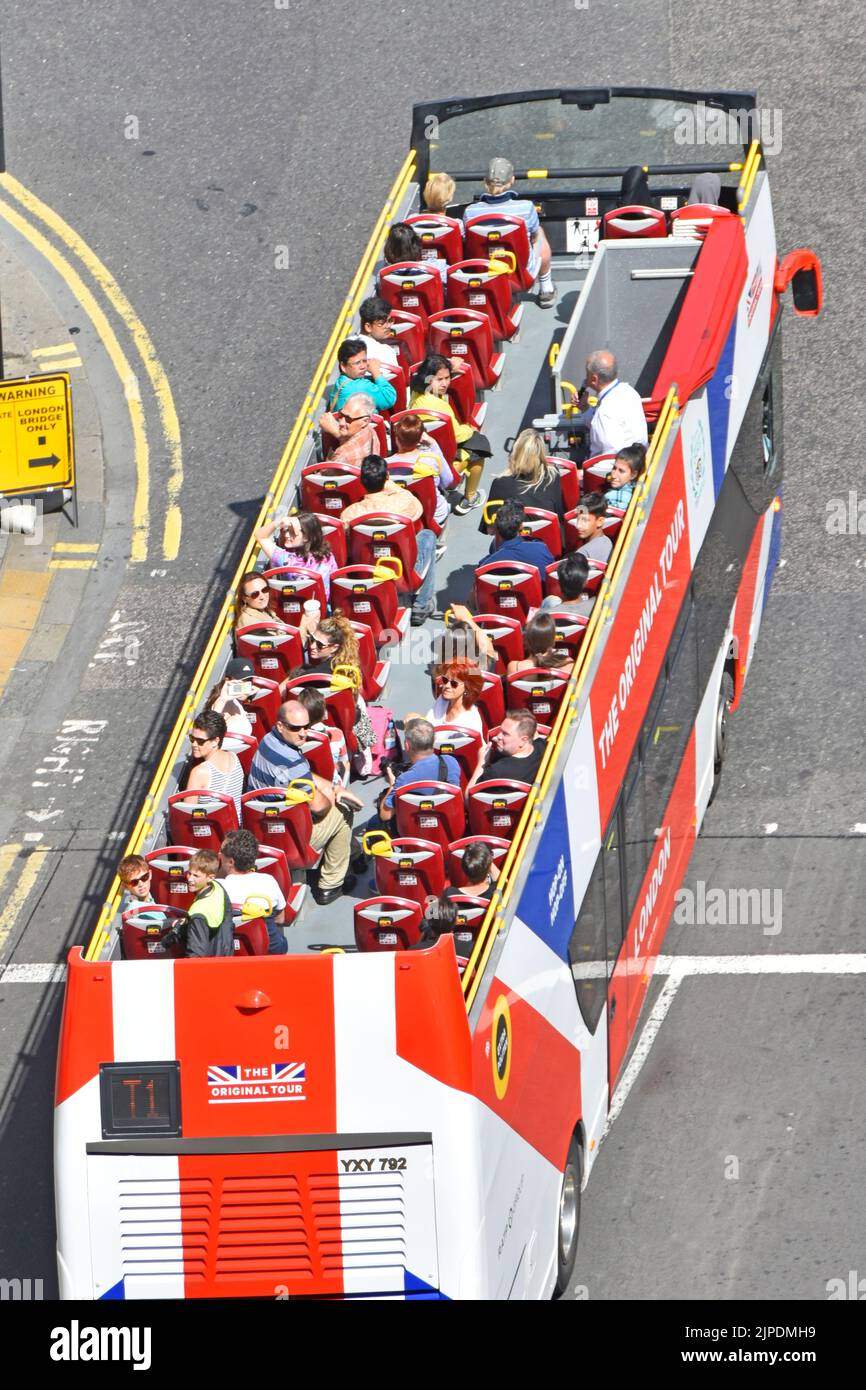 Aerial birds eye view looking town from above at top deck of red white & blue London sightseeing tour bus on sunny day full of tourists England UK Stock Photo