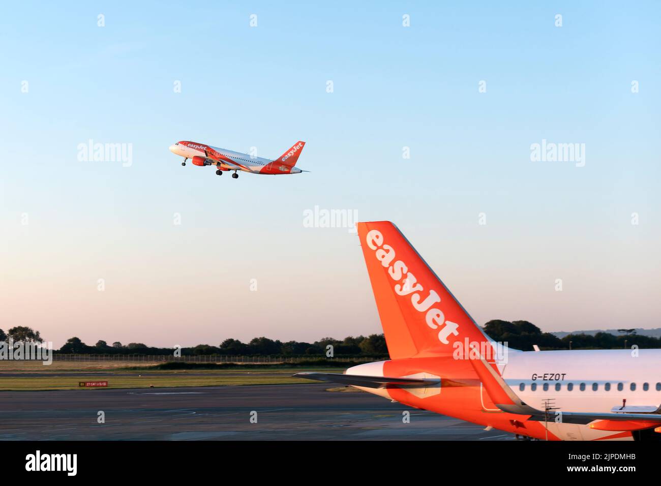 An EasyJet plane taking off from Bristol airport.  Another EasyJet plane is parked on the runway. The companies logo and branding are clearly shown. Stock Photo