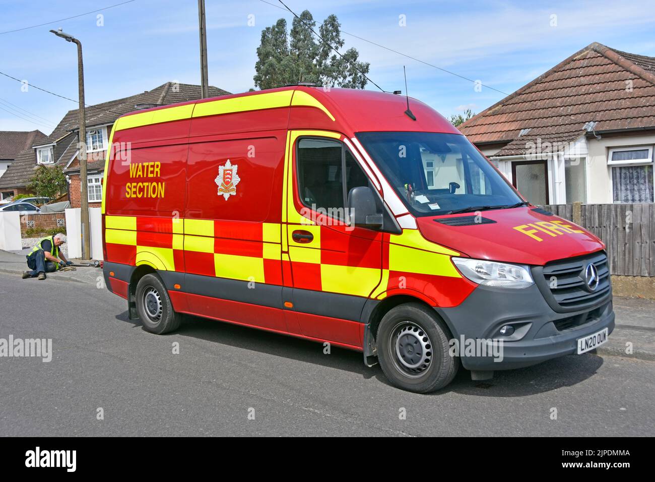 Fire brigade van driver laying on pavement removing stuck cover underground street fire hydrant Essex Fire and Rescue Service Water Section England UK Stock Photo