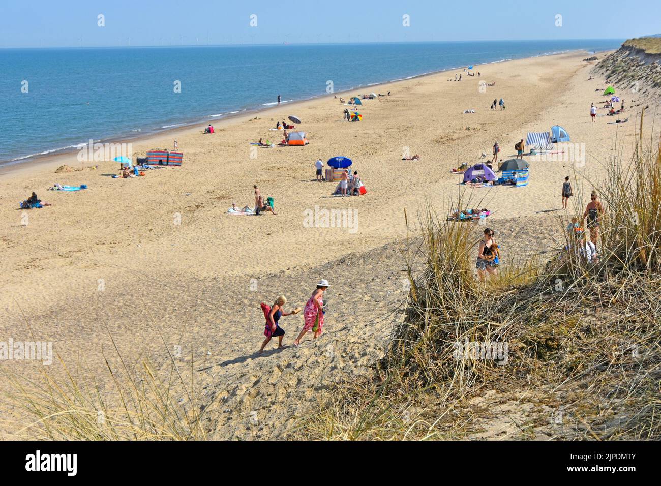 Winterton-on-Sea people on sandy sunbathing beach beyond dunes  coarse grass planted to help reduce erosion from North Sea storms Norfolk England UK Stock Photo