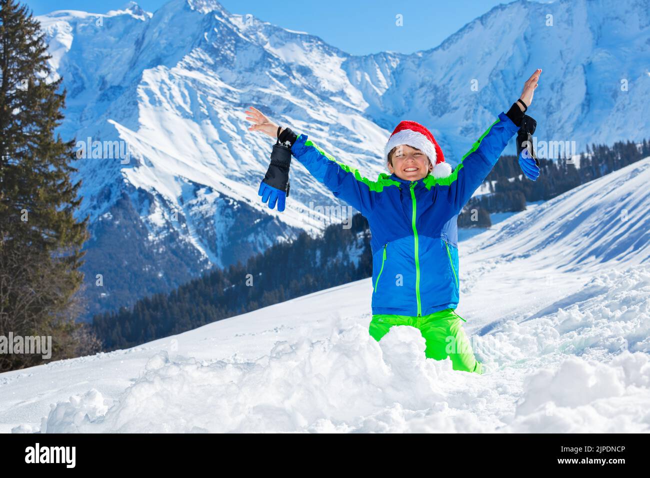 Boy with Santa hat and big smile stand in snow over mountains Stock Photo