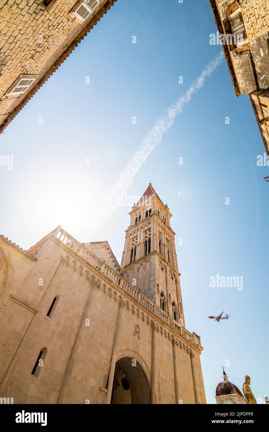 View of cathedral of St Lawrence, Trogir - Croatia. Down to up look to beautiful ancient church tower. The airplane is landing to Split airport. Aircr Stock Photo