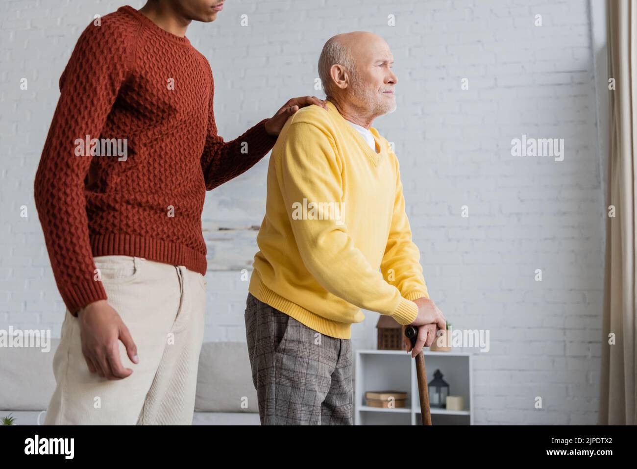 African american grandson hugging sad grandpa with walking cane at home Stock Photo