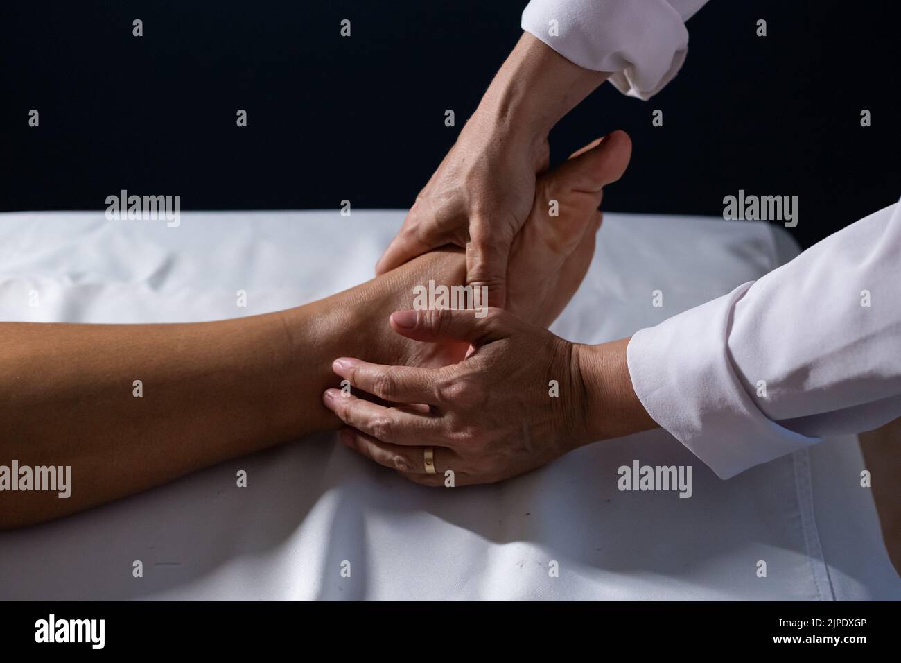 Goiânia, Goias, Brazil – July 18, 2022: Detail of masseuse hands applying therapeutic massage on the foot of a patient who is lying. Stock Photo
