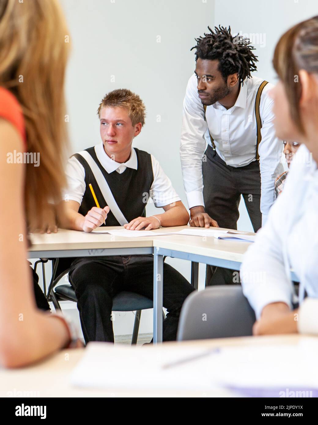 Teenage Students, candid classroom. A genuine class scene with a teacher and pupil engaged with a third character. From a series of related images. Stock Photo