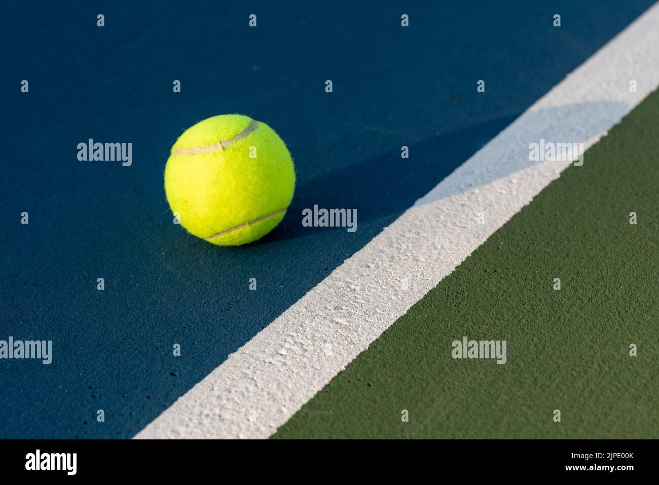 Yellow tennis ball near baseline on a new blue tennis court with green