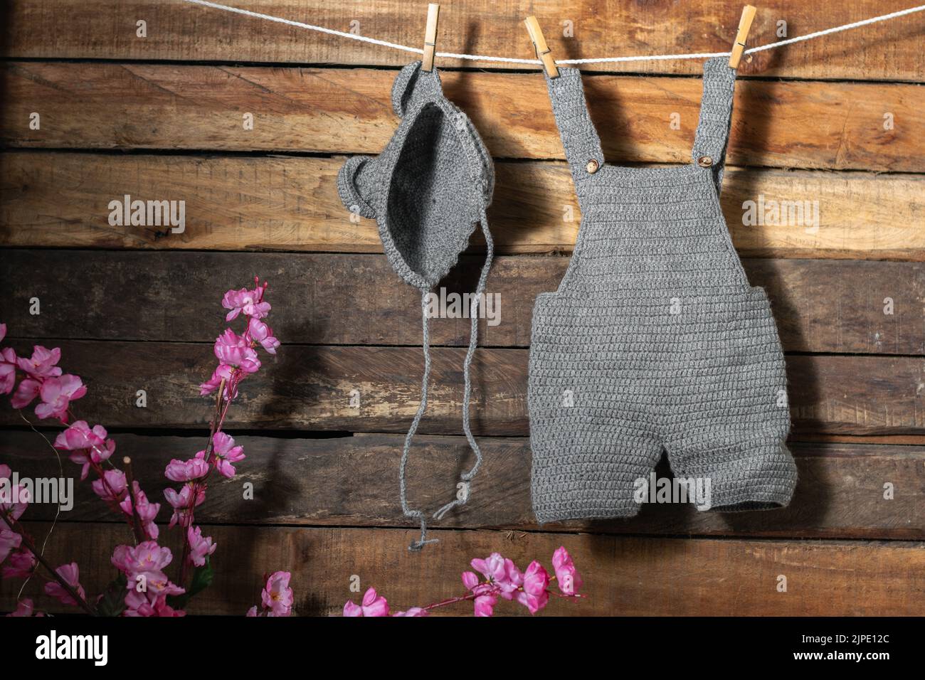 baby clothes hanging from a clothesline rope tied with wooden hooks, overalls and hat with ears knitted in the technique of hand crochet, on a backgro Stock Photo