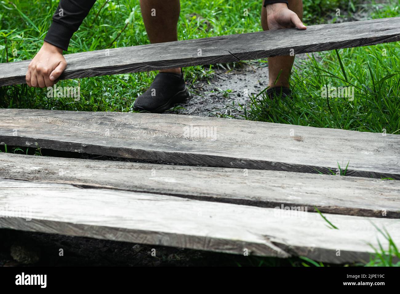 young latino man of limited economic resources, grabbing some old wooden boards to place them on the ground to build his house. boy putting boards on Stock Photo