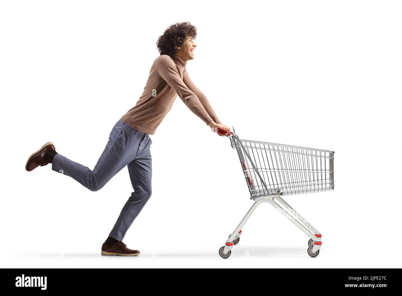 Full length profile shot of a young man running with an empty shopping cart isolated on  white background Stock Photo