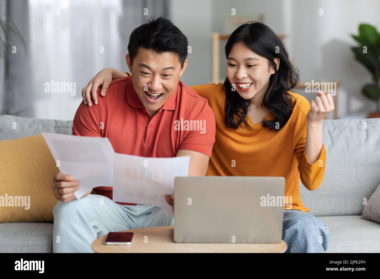 Emotional asian spouses reading papers, using laptop Stock Photo
