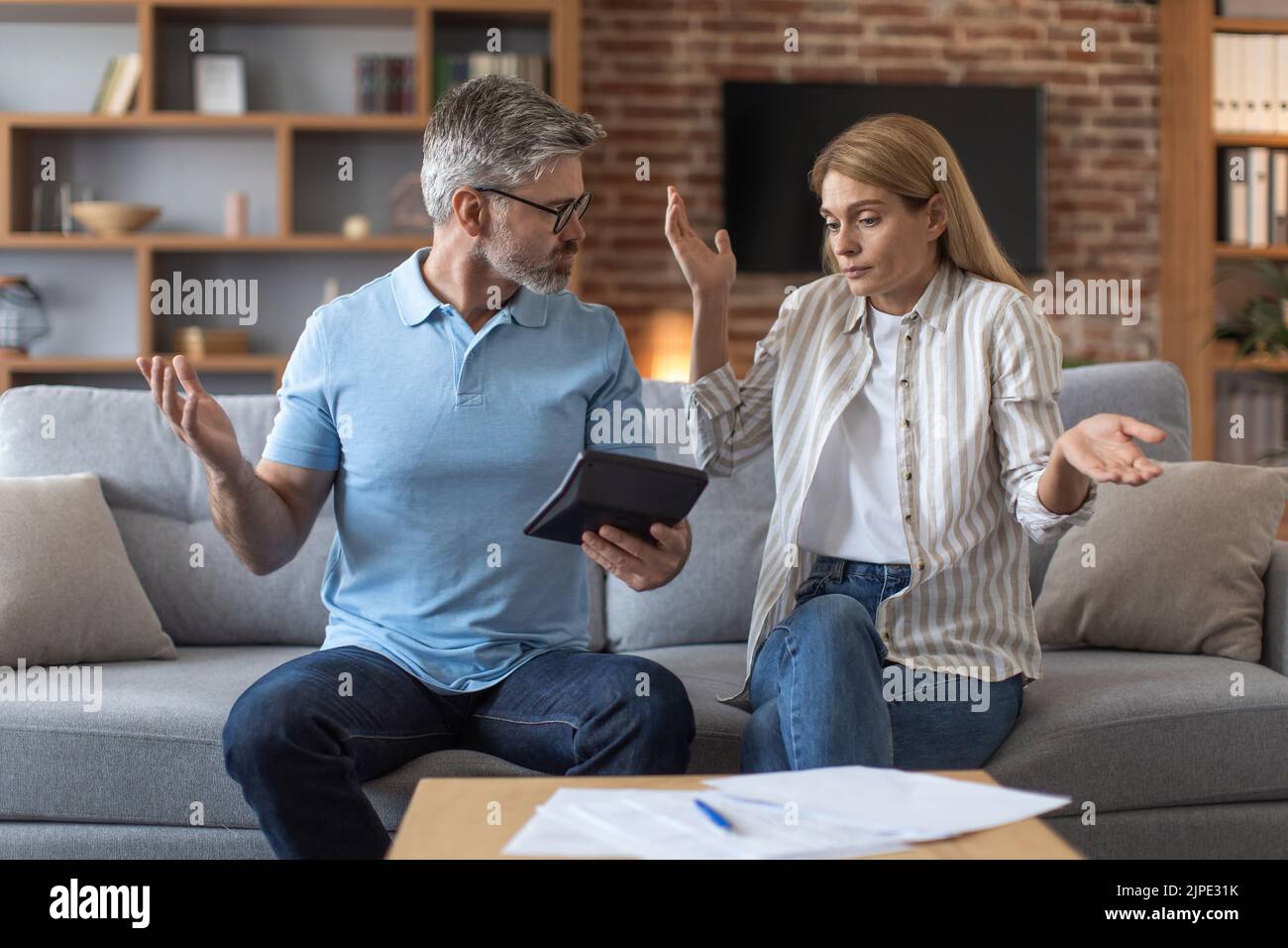 Sad adult caucasian family work with documents and tablet, quarreling in room interior Stock Photo