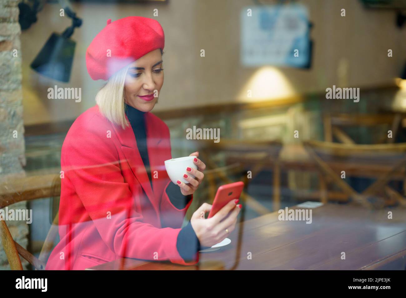 Through glass of woman with coffee browsing smartphone Stock Photo