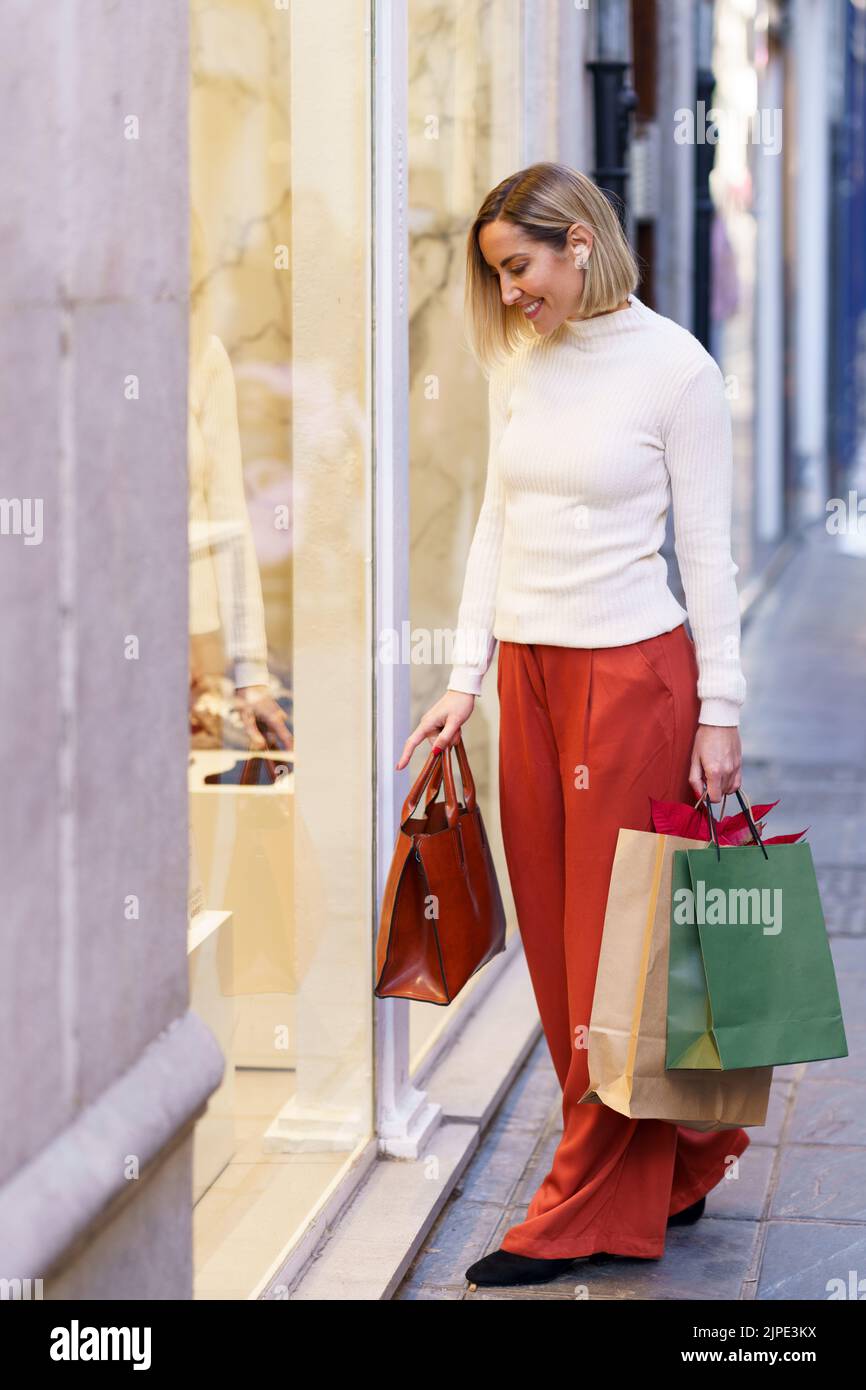Female shopper with bags looking through shop showcase Stock Photo